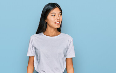 Beautiful young asian woman wearing casual white t shirt looking away to side with smile on face, natural expression. laughing confident.