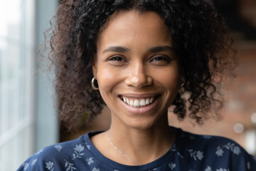Close up head shot of happy millennial African American woman with fine face skin and white teeth looking at camera, smiling, feeling joy. Beautiful Black girl portrait. Skincare, beauty care concept