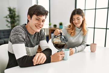 Young caucasian couple having breakfast pouring coffee on cup at home.