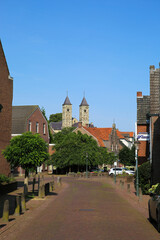 Fototapeta premium Sint Odilienberg, Netherlands - 9. July 2021: View over street beyond houses on roman basilica from 11th century against blue summer sky