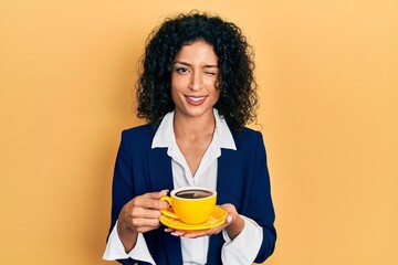 Young latin girl wearing business style drinking cup of coffee winking looking at the camera with sexy expression, cheerful and happy face.