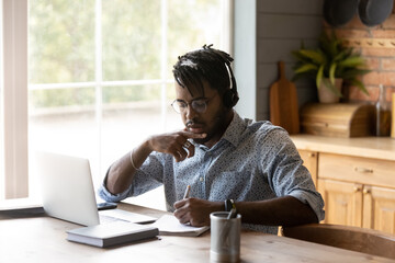 Focused African American student guy in headphones watching learning webinar, virtual training on...