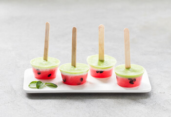 Obraz na płótnie Canvas Mini watermelon ice cream with kiwi on a wooden stick on a ceramic plate on a light background