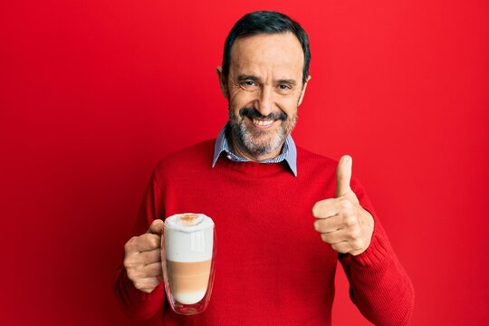 Middle age hispanic man drinking a cup of cappuccino coffee smiling happy and positive, thumb up doing excellent and approval sign