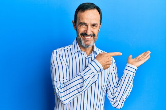 Middle age hispanic man wearing casual clothes amazed and smiling to the camera while presenting with hand and pointing with finger.