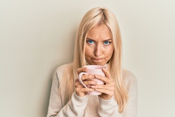 Young blonde woman drinking a cup of coffee skeptic and nervous, frowning upset because of problem. negative person.