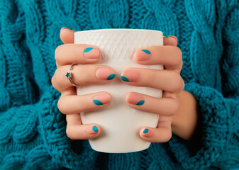 Womans hands with blue manicure holding cup. Trendy winter autumn nail design