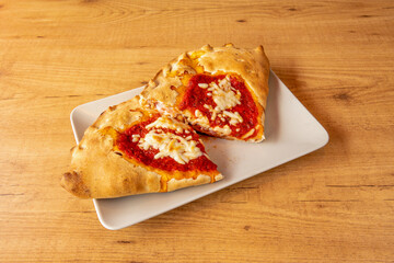 delicious calzone stuffed with ham, cheese and tomato cooked in a stone oven on a wooden table