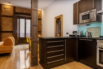 Modern kitchen corner in vintage building with metal-reinforced wooden columns, exposed brick walls and wooden carpentry in a vacation rental apartment