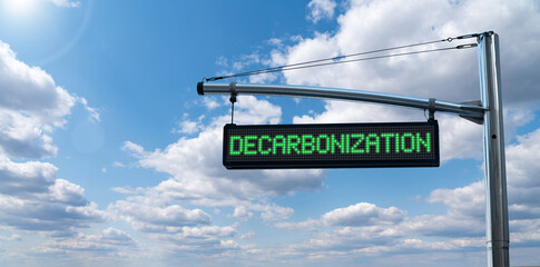 Road information board with text DECARBONIZATION on a background of blue sky. Carbon neutrality...