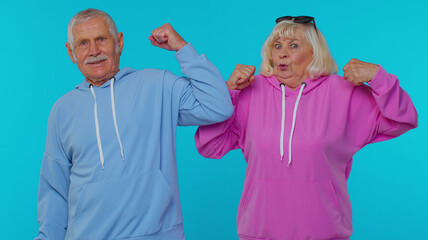 We are strong and independent. Cheerful senior man woman grandparents showing biceps and looking confident, feeling power strength to fight for rights, energy to gain success win on blue background