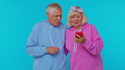 Excited happy joyful senior couple man woman grandparents use mobile cell phone typing browsing say wow yes, found out great big win news doing winner gesture. Elderly mature grandfather grandmother