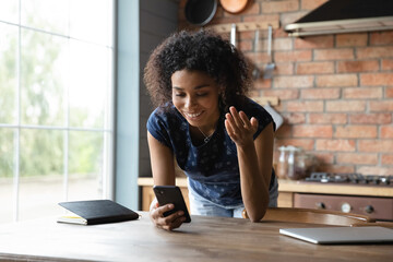 Smiling excited African American remote worker chatting with client online on smartphone, making...