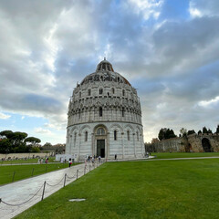 Obraz premium Baptisterium neben dem Dom in Pisa auf dem Platz Piazza dei Miracoli. Grüner Rasen und bewölkter Himmel.