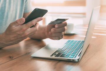Online shopping from home, man using laptop computer, mobile smart phone and credit card to purchase