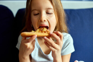 Cute little girl sitting on couch and eating piece of italian Pizza at home