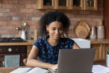 Happy millennial Black distance employee working at laptop from home kitchen, watching virtual presentation, chatting online, making video call. Remote student girl attending virtual class, webinar