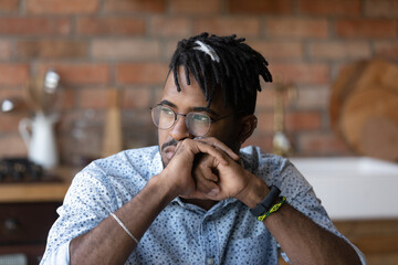 Thoughtful millennial African American man looking at window away in deep thoughts, thinking over...
