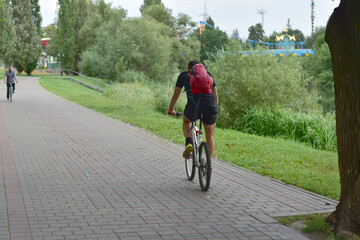 The photo shows a young athlete riding a bicycle along a park track.