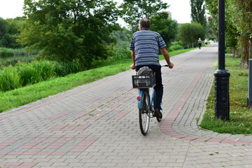 The picture shows an elderly man riding a bicycle along a park path.