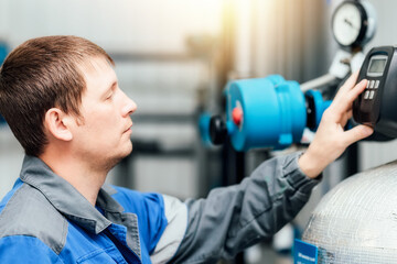 A man in work clothes checks the sensors of the boiler or compressor station. System monitoring. Engineer at work at an industrial facility indoors. A real scene while working.