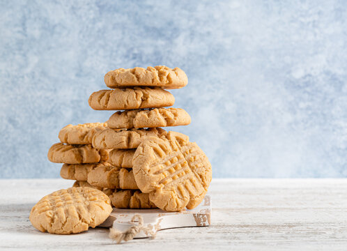Peanut butter cookies stack on wooden cutting board. Traditional american dessert, nutrition snack, dessert or breakfast food. Blue and white background. Closeup food. Criss cross patterned biscuits.