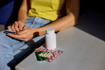 Unrecognizable woman sitting on sofa with blister pack of pills using online pharmacy store