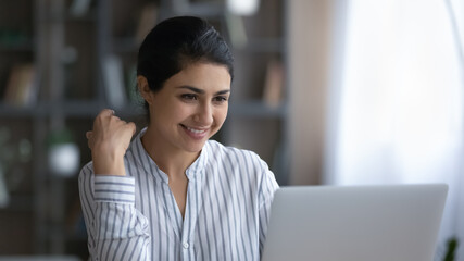 Smiling young Indian woman businesswoman work online on laptop at home office, consult client on web. Happy millennial mixed race female student study distant on computer. Technology concept.