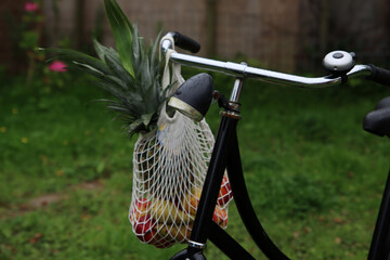 Cotton mesh bag full of fresh fruits and vegetables on bicycle wheel. Close up photo of black bicycle. Healthy lifestyle concept. 