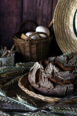 Handmade fresh wheat bread on a wicker tray, wheat ears around, straw hat and wicker bag on background