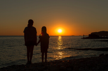 Silhouettes of children against the sunset on the seashore. The concept of family values.