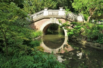 Petit pont enjambant le ruisseau du parc Monceau à Paris, et son reflet dans l'eau, au milieu de la végétation du jardin (France)
