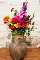 Bouquet of flowers in antique rustic clay jug against white brick wall