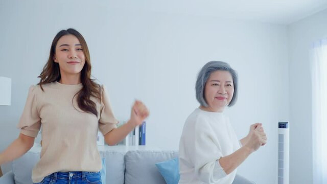 Asian funny senior old mom and daughter dance together in living room. 