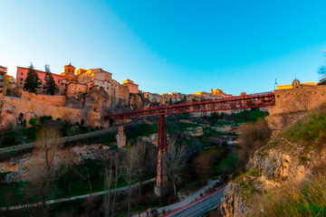 Fototapeta na wymiar Cityscape in old town changing light at sunset; Hanging houses with old town hanging over mountain and red bridge of San Pablo de Cuenca, world heritage site, Spain. Horizontal view
