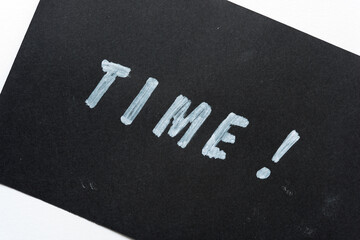 the word "time!" stencilled in white marker on a black paper background