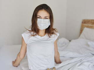 a woman in a medical mask in a T-shirt and shorts sits on the bed 
