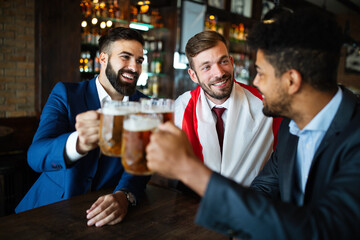 Men fans screaming and watching football on TV and drink beer in a pub