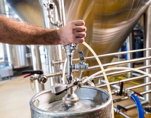Young male brewer in leather apron supervising the process of beer fermentation at modern brewery factory