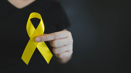 World suicide prevention day. Human hands holding yellow ribbon awareness symbol for preventing suicide on black background. Mental health care concept. - obrazy, fototapety, plakaty