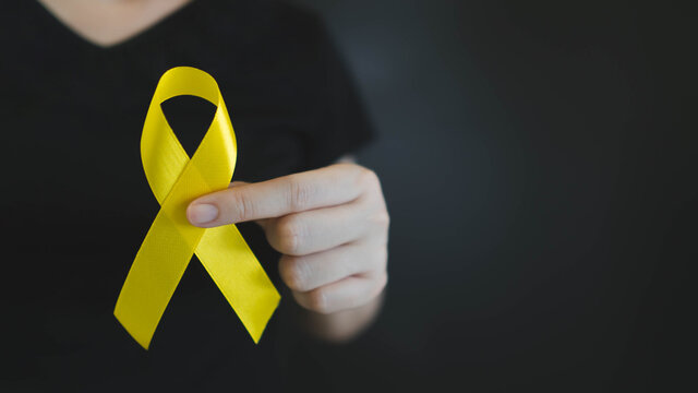 World suicide prevention day. Human hands holding yellow ribbon awareness symbol for preventing suicide on black background. Mental health care concept.