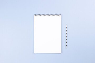 Open spiral notebook with blank white page and pencil on light gray desk background. Top view, copy space for text