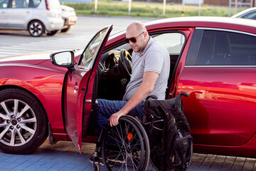 Naklejka na ściany i meble Young handicapped driver getting in red car fom wheelchair