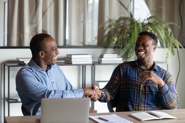 Overjoyed African American male business partners shake hands close deal after success office...