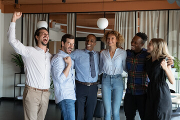 Excited diverse multiethnic businesspeople feel euphoric celebrate mutual team win or victory in office. Smiling overjoyed multiracial employees triumph with good business results or shared success.