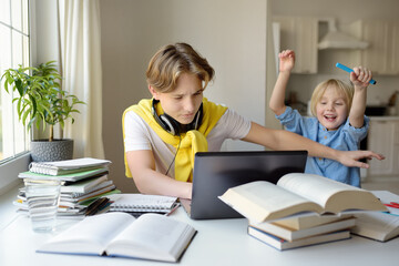 Teenager boy study at home and his younger brother screams and interrupts him. Online education and...
