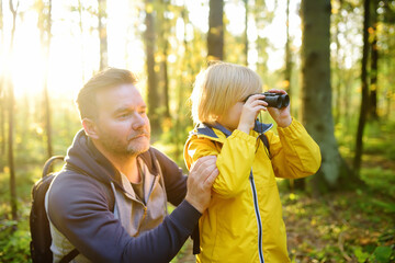 Cute schoolchild and his mature father hiking together and exploring nature. Child looking through...
