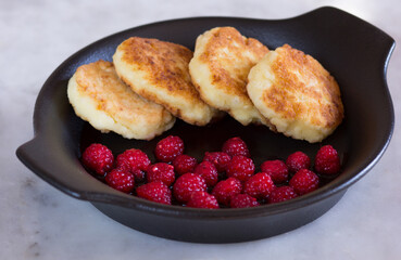 Close up fried homemade syrniki with fresh raspberry on black plate on marble background