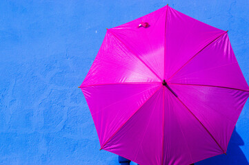 Paraguas abierto color rosa sobre una pared azul añil