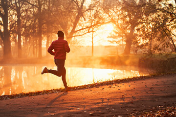 Man running at autumn morning in park during sunrise